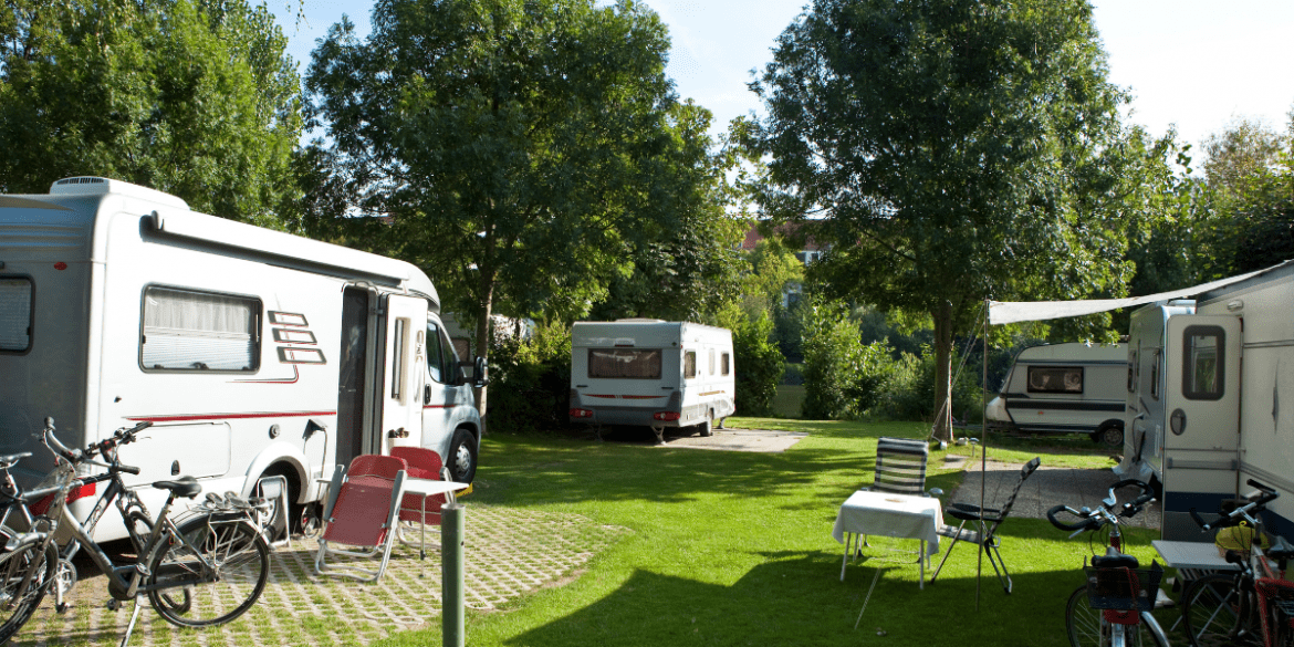 4 RVs parked in a circle at an RV park with grass between and surrounded by trees