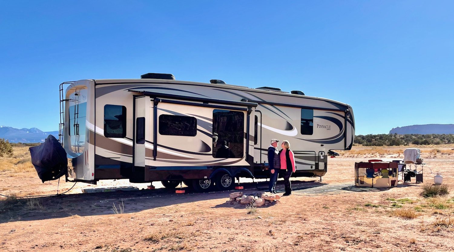 couple living in an RV standing in front of the RV in the desert