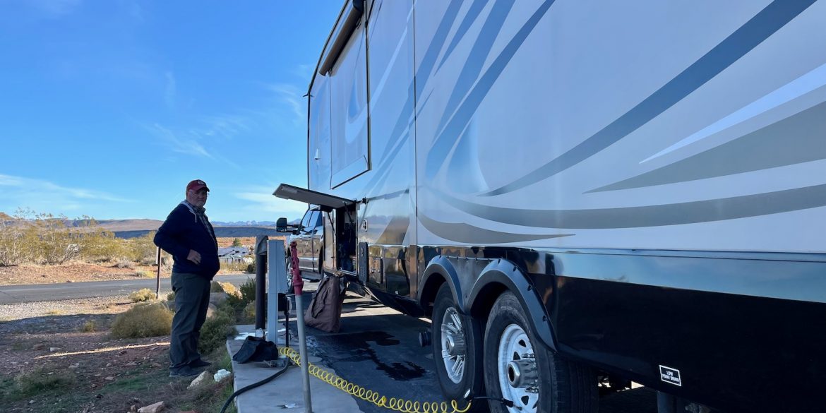 man liviing in an RV standing beside jayco pinnacle fifth wheel adding air to tires before traveling.